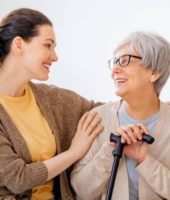 Elderly woman with cane looking and smiling at caregiver woman.