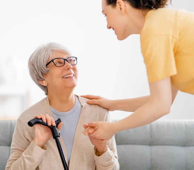 Elderly woman with cane smiling up at employee helping her